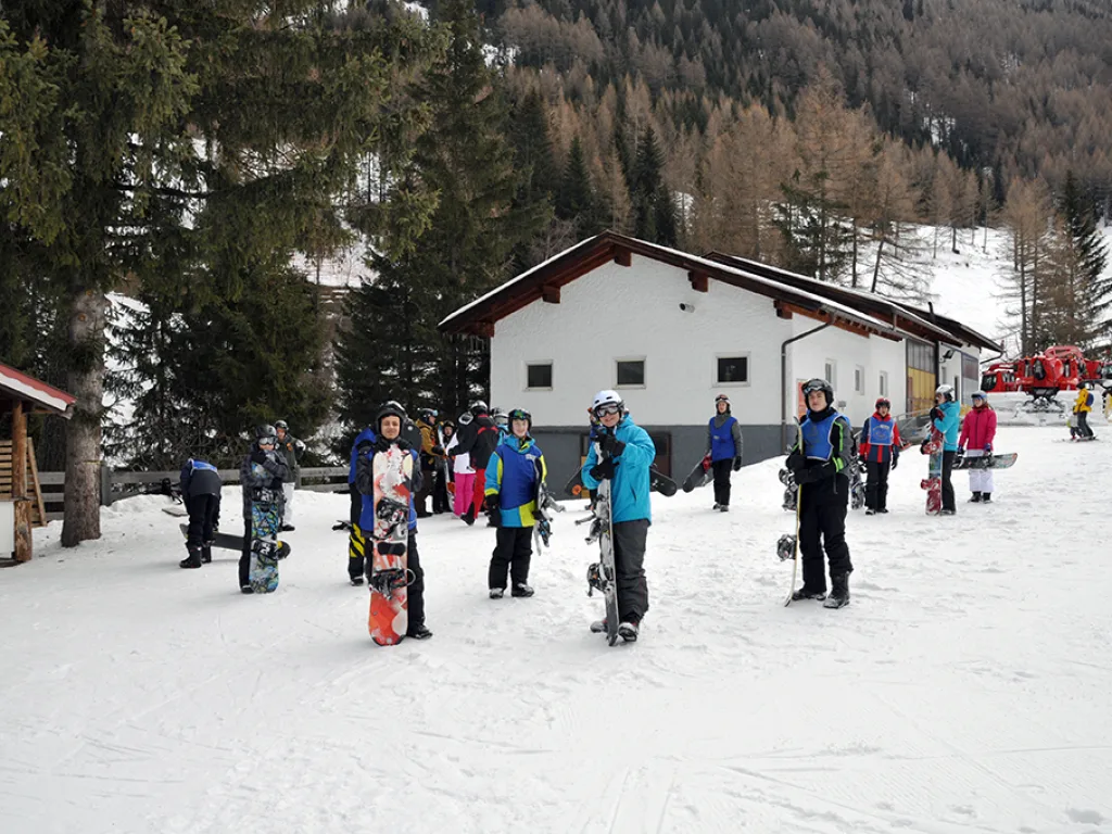 Jugendliche mit Snowboards stehen vor einem Haus im Schnee.